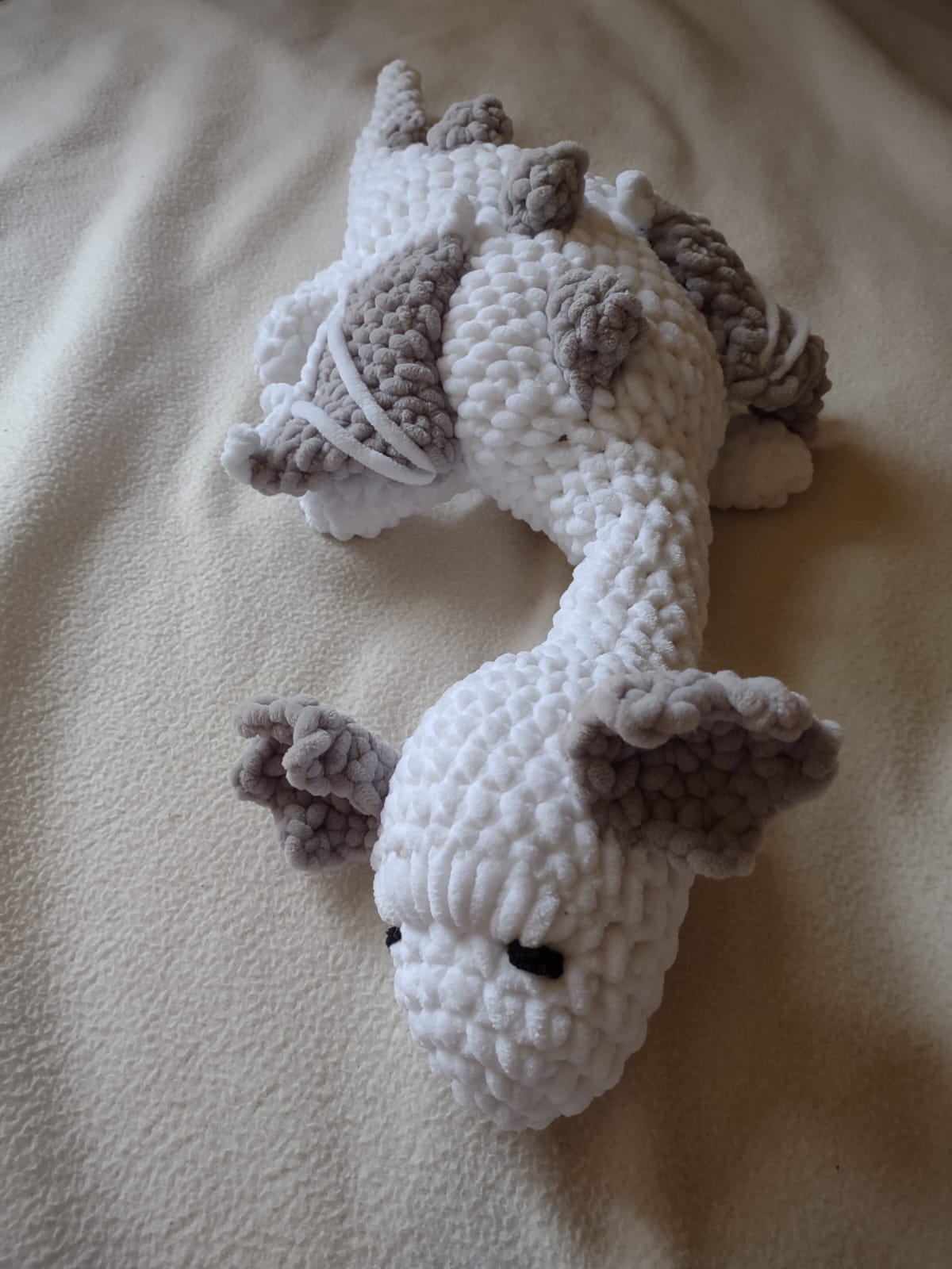 An image of a crocheted (amigurumi) dragon using chinelle yarn. The dragon's body is white, with ears, horns and wings of gray.