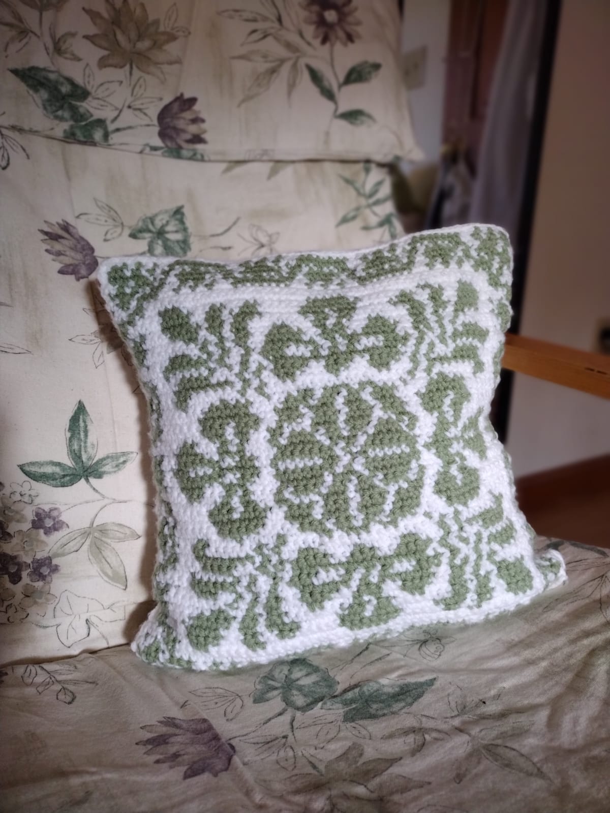 Image of a small (~14x14in) pillow with an elaborate crocheted green and white motif.